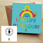 Colourful greeting card with a rainbow, a caterpillar and a strawberry, with the text "Live Life in Colour" on a blue background. The card is on a brown envelope on a wooden table.