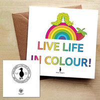 Colourful greeting card with a rainbow, a caterpillar and a strawberry, with the text "Live Life in Colour" on a white background. The card is on a brown envelope on a wooden table.