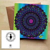 Colourful Mandala Design in blues, greens and purples. Card is on a brown envelope on a wooden table.