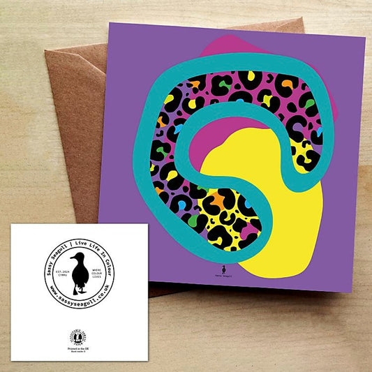 Colorful abstract animal print design on a purple card with a brown envelope on a wooden table.
