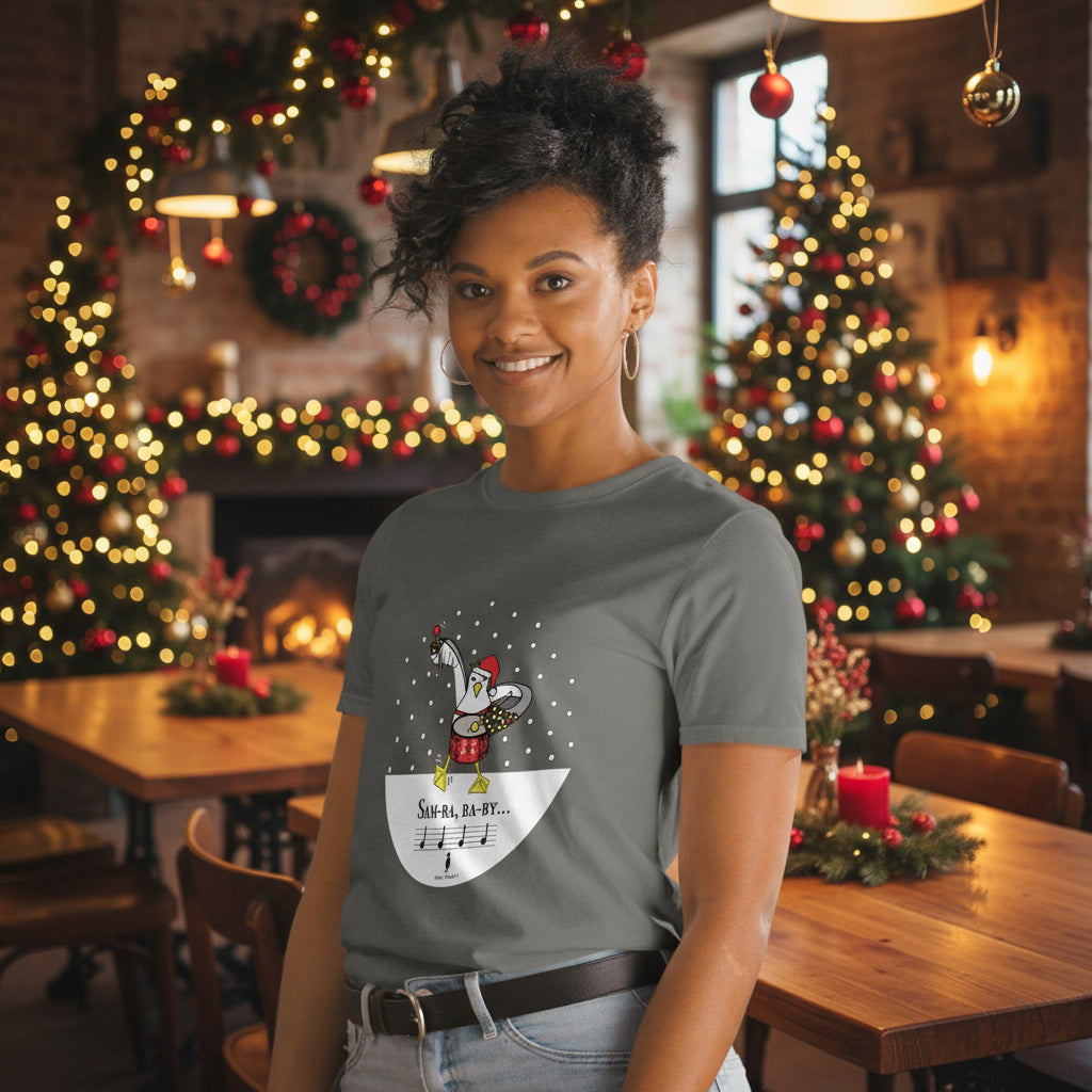 Woman wearing a charcoal grey 100% cotton samba drumming seagulll in the snow Christmas t-shirt with the text Samba Baby in a rustic cafe filled with red, green and gold Christmas decorations
