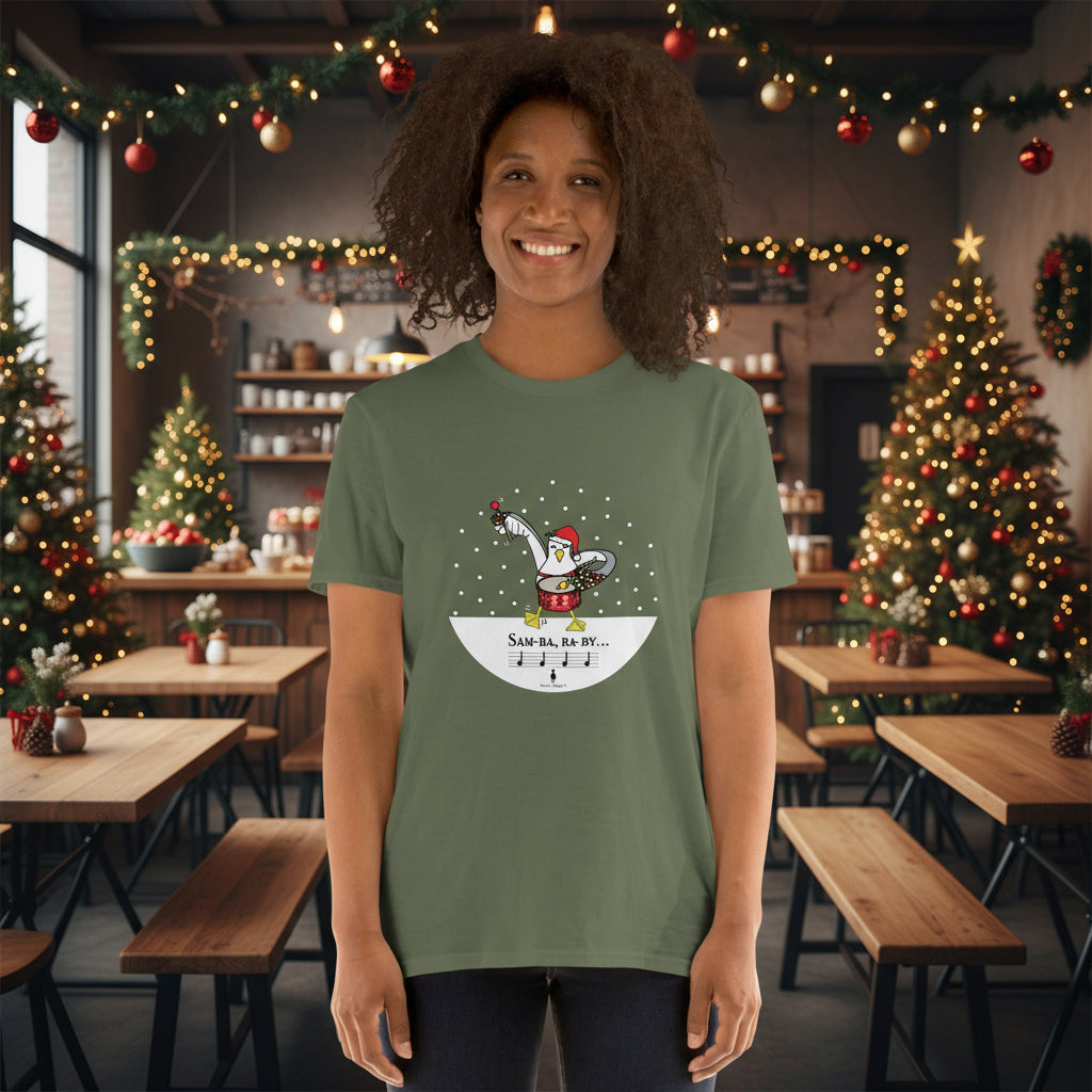 Woman wearing a khaki green 100% cotton samba drumming seagulll in the snow Christmas t-shirt with the text Samba Baby in a rustic cafe filled with red, green and gold Christmas decorations