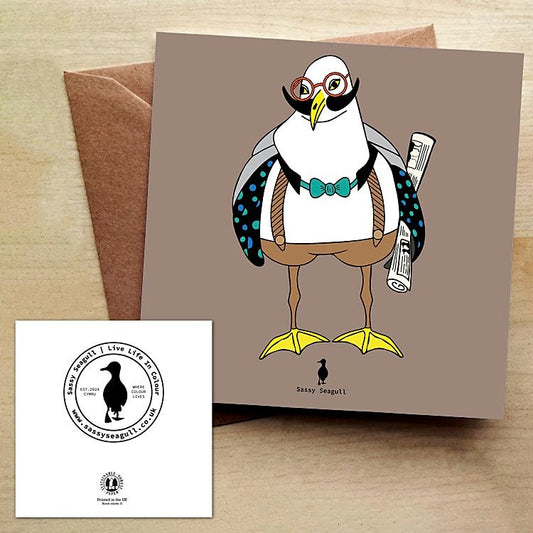 Greeting card with a stylized seagull wearing glasses and a bow tie, accompanied by a brown envelope on a wooden surface.