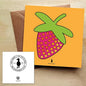 Card with a colourful and bold strawberry print on an orange background, with a brown envelope on a wooden table